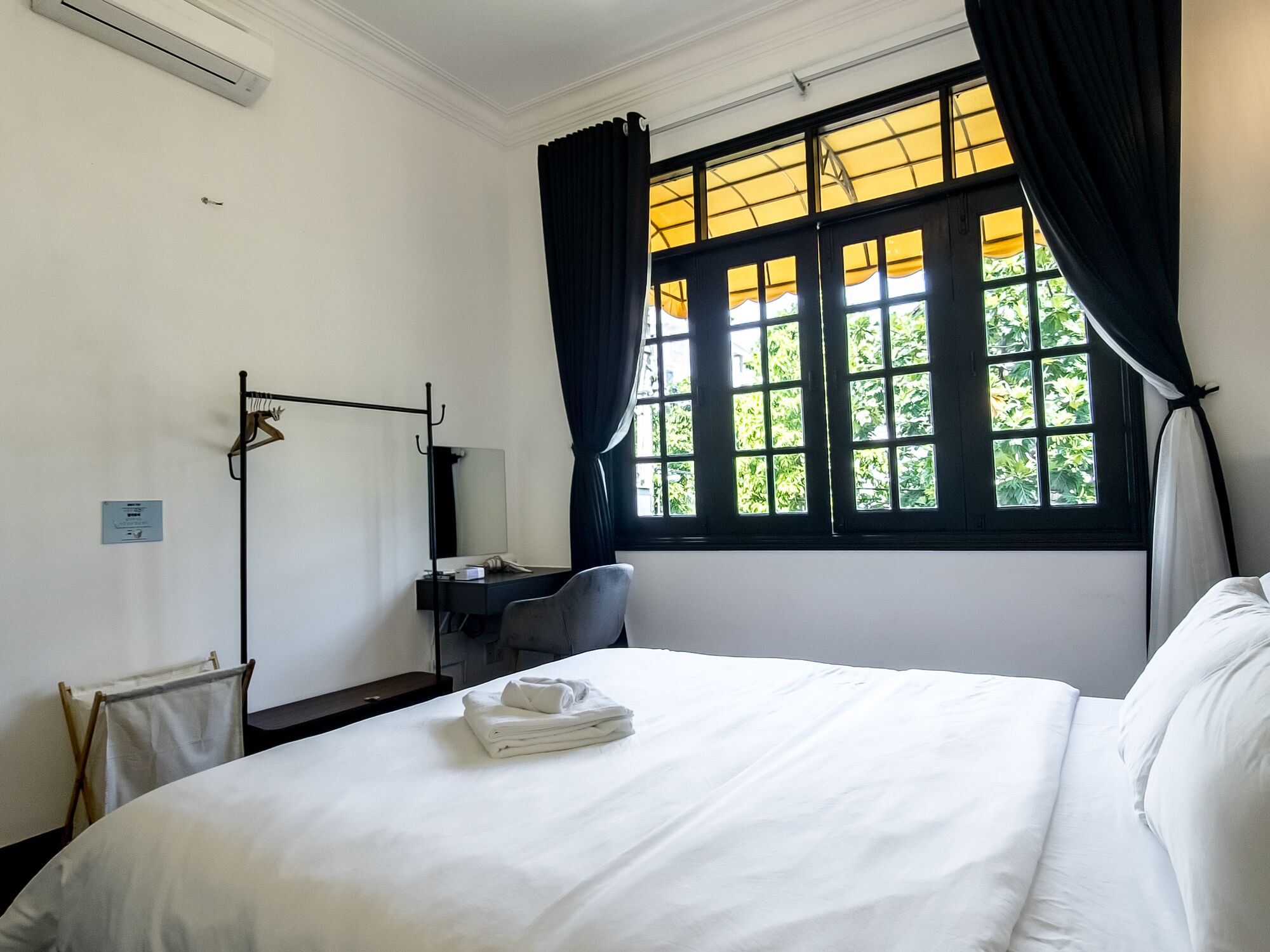 Une chambre d’hôtel avec un lit, un bureau, une chaise, une fenêtre avec des rideaux et un radiateur.