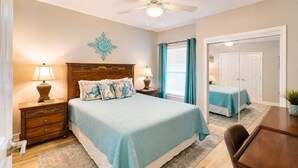A bedroom with a bed, bedside tables, a mirror, a ceiling fan, and a door leading to another room. - Legacy Tower II 802 | Stunning Coastal Views! (Gulfport)