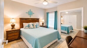 A bedroom with a bed, bedside tables, a mirror, a ceiling fan, and a door leading to another room. - Legacy Tower II 802 | Stunning Coastal Views! (Gulfport)