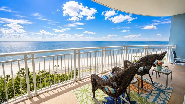 A balcony with wicker furniture, a patterned rug, and a view of the ocean. - Legacy Tower II 802 | Stunning Coastal Views! (Gulfport)