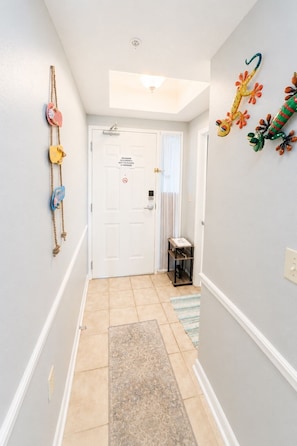 A hallway with a white door, a small shelf, and a wall-mounted decoration. - Legacy Tower II 802 | Stunning Coastal Views! (Gulfport)