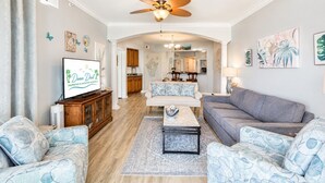A living room with a television, sofas, a coffee table, and a ceiling fan. - Legacy Tower II 802 | Stunning Coastal Views! (Gulfport)