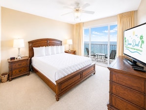 A hotel room with a large bed, two bedside tables, a television, a ceiling fan, and a balcony with a view of the ocean. - Legacy Tower II 708 | Overlooking the Beautiful Gulf Coast! (Gulfport)
