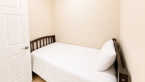 Quarto com uma cama de solteiro, cabeceira de madeira, porta branca e ventilador de teto.