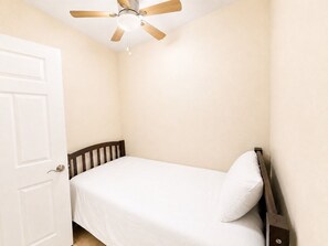 Ein Schlafzimmer mit einem Einzelbett, einem Holz-Kopfteil, einer weißen Tür und einem Deckenventilator.