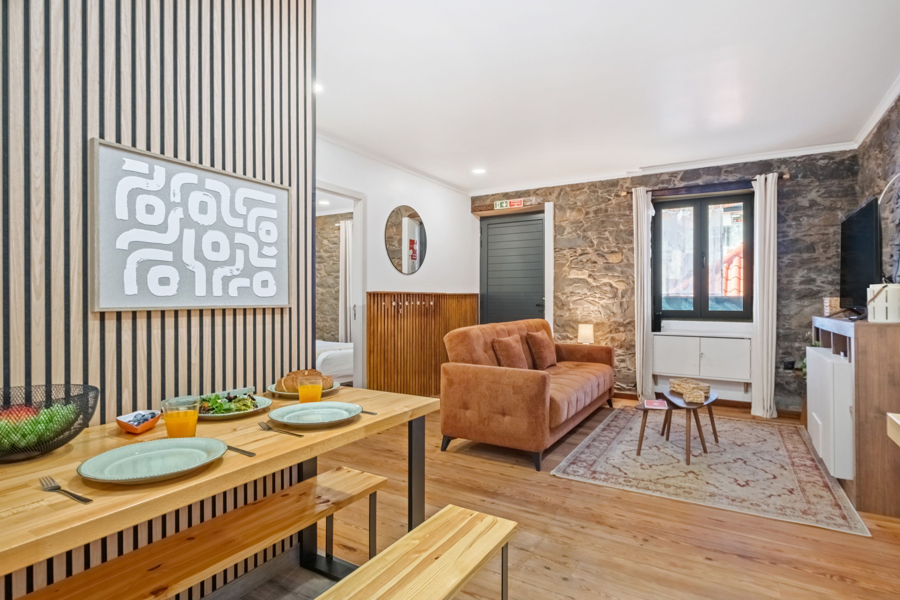 Een moderne woonkamer met een bank, een eettafel met bankjes en een stenen muur.