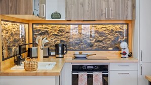 A modern kitchen with a stone backsplash, a coffee machine, a kettle, and a stove. - Stone House Rochinha by Homie (Funchal)