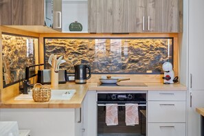 A modern kitchen with a stone backsplash, a coffee machine, a kettle, and a stove. - Stone House Rochinha by Homie (Funchal)