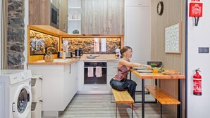 A modern kitchen with a built-in oven, a microwave, and a coffee maker. There is a wooden bench and a small table with a person sitting at it. - Stone House Rochinha by Homie (Funchal)