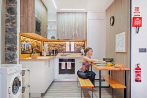 A modern kitchen with a built-in oven, a microwave, and a coffee maker. There is a wooden bench and a small table with a person sitting at it. - Stone House Rochinha by Homie (Funchal)