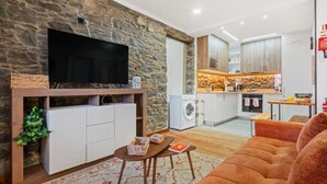 A modern living room with a stone wall, a flat-screen TV, a sofa, and a small table with decorative items. - Stone House Rochinha by Homie (Funchal)