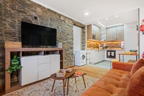A modern living room with a stone wall, a flat-screen TV, a sofa, and a small table with decorative items. - Stone House Rochinha by Homie (Funchal)