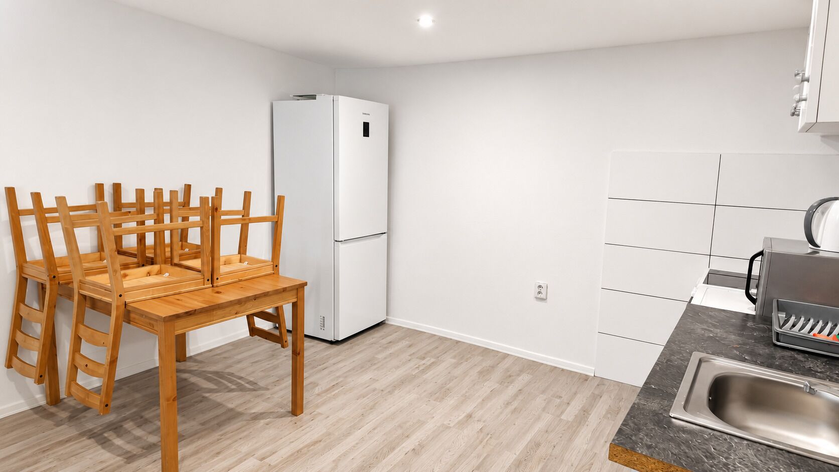 Una cocina compacta con refrigerador incorporado, una mesa de comedor de madera con sillas y un lavamanos moderno.