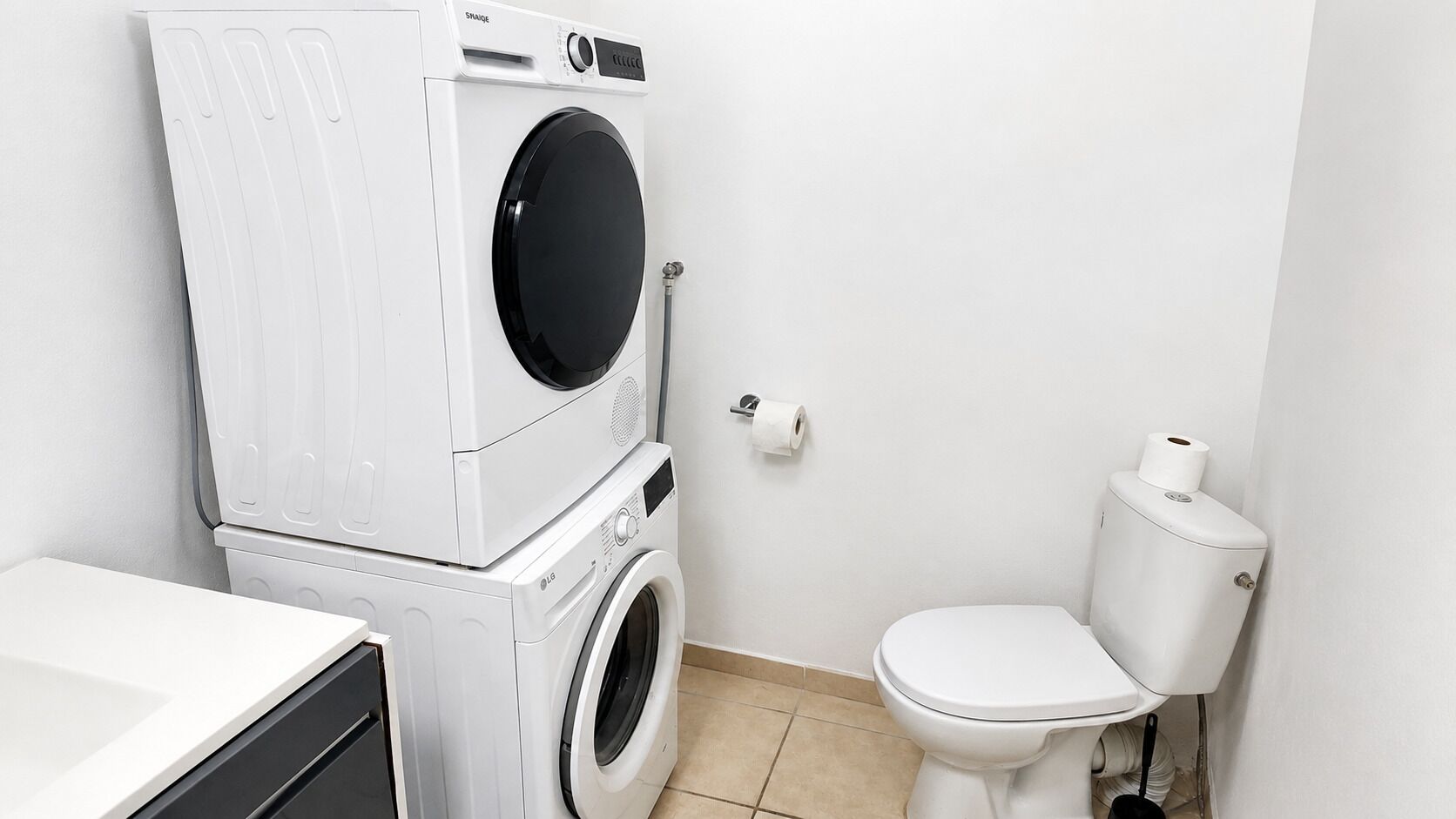 A compact laundry room with stacked washing machines and a toilet.