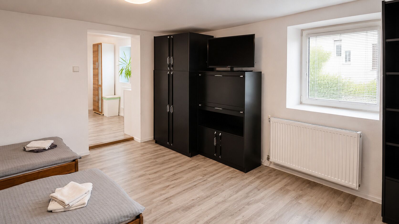 A room with a bed, a black wardrobe, a television, and a window with blinds.
