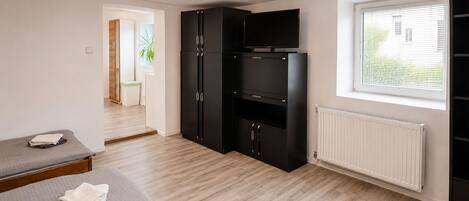 A room with a bed, a black wardrobe, a television, and a window with blinds.