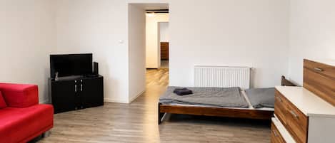A compact bedroom with a bed, a red sofa, a black entertainment unit, and a wooden dresser.