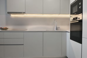 A modern kitchen with white cabinetry, a stainless steel sink, and built-in appliances including a microwave and oven. - SUNSET SAILORS cozy apartment (Benidorm)