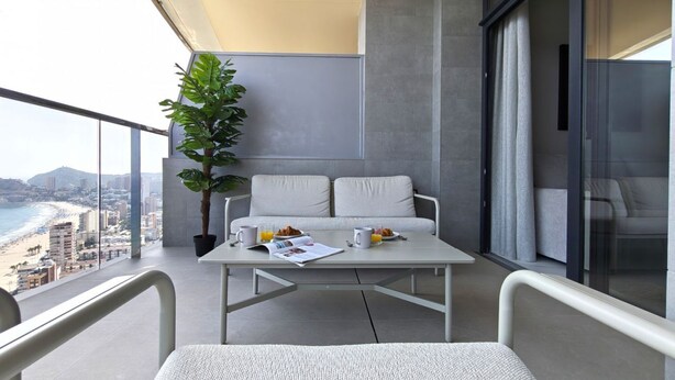 A balcony with a table, chairs, a plant, and a view of the beach and cityscape. - SUNSET SAILORS cozy apartment (Benidorm)