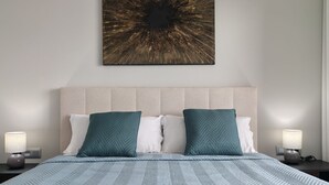 A neatly made bed with a patterned blue bedspread, two pillows, and a wall-mounted abstract artwork. - SUNSET SAILORS cozy apartment (Benidorm)