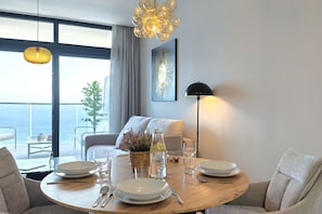 A dining area with a round table set for four, a potted plant, and a view of the sea through large windows. - SUNSET SAILORS cozy apartment (Benidorm)