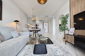 A modern living room with a sofa, a coffee table, and a dining area with chairs. - SUNSET SAILORS cozy apartment (Benidorm)