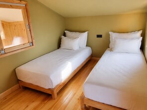 Ein Zimmer mit zwei Einzelbetten, Holzboden, einem Schrank aus Holz und einem Spiegel an der Wand.
