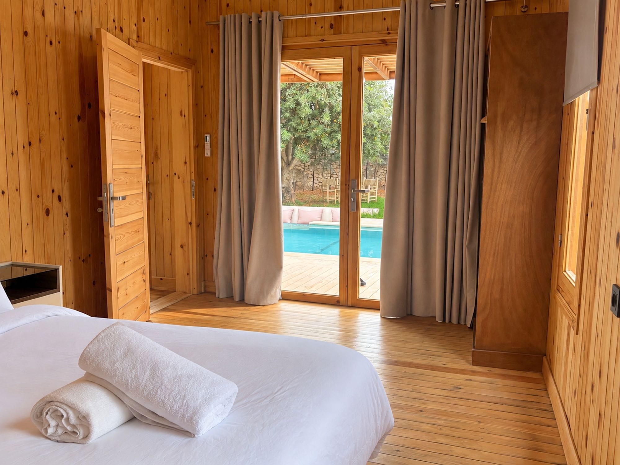 A wooden room with a bed, a sliding glass door to a pool area, and a wooden floor.