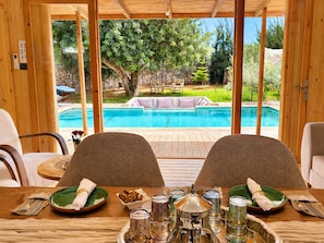 Ein Essbereich mit Blick auf einen Swimmingpool, Holzmöbel und ein Tisch, gedeckt mit Tellern, Gläsern und Besteck.
