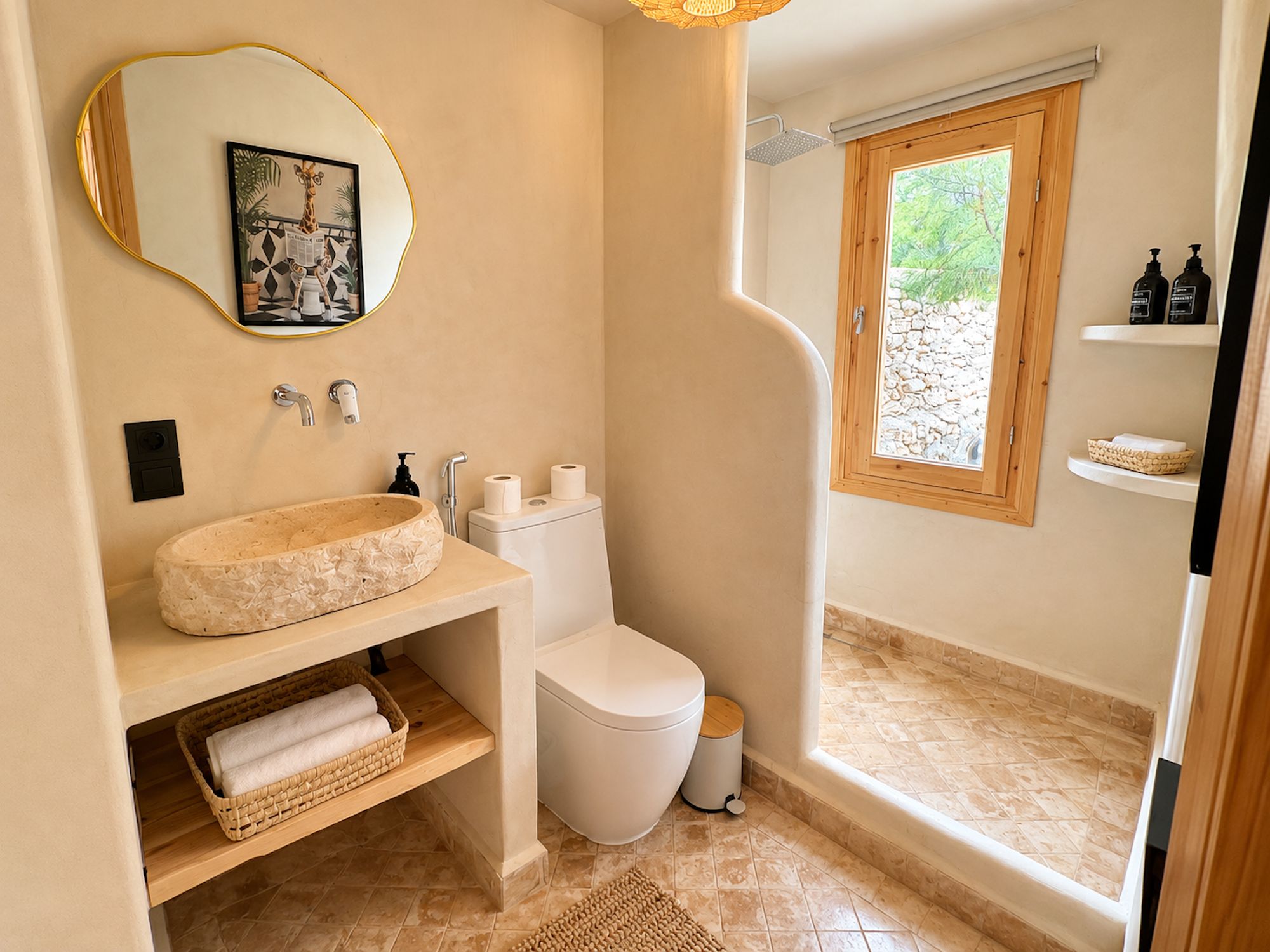 A bathroom with a round sink, toilet, and a window with a view of greenery.