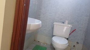 Pieni kylpyhuone, jossa on wc, pesuallas ja vihreä matto lattialla.