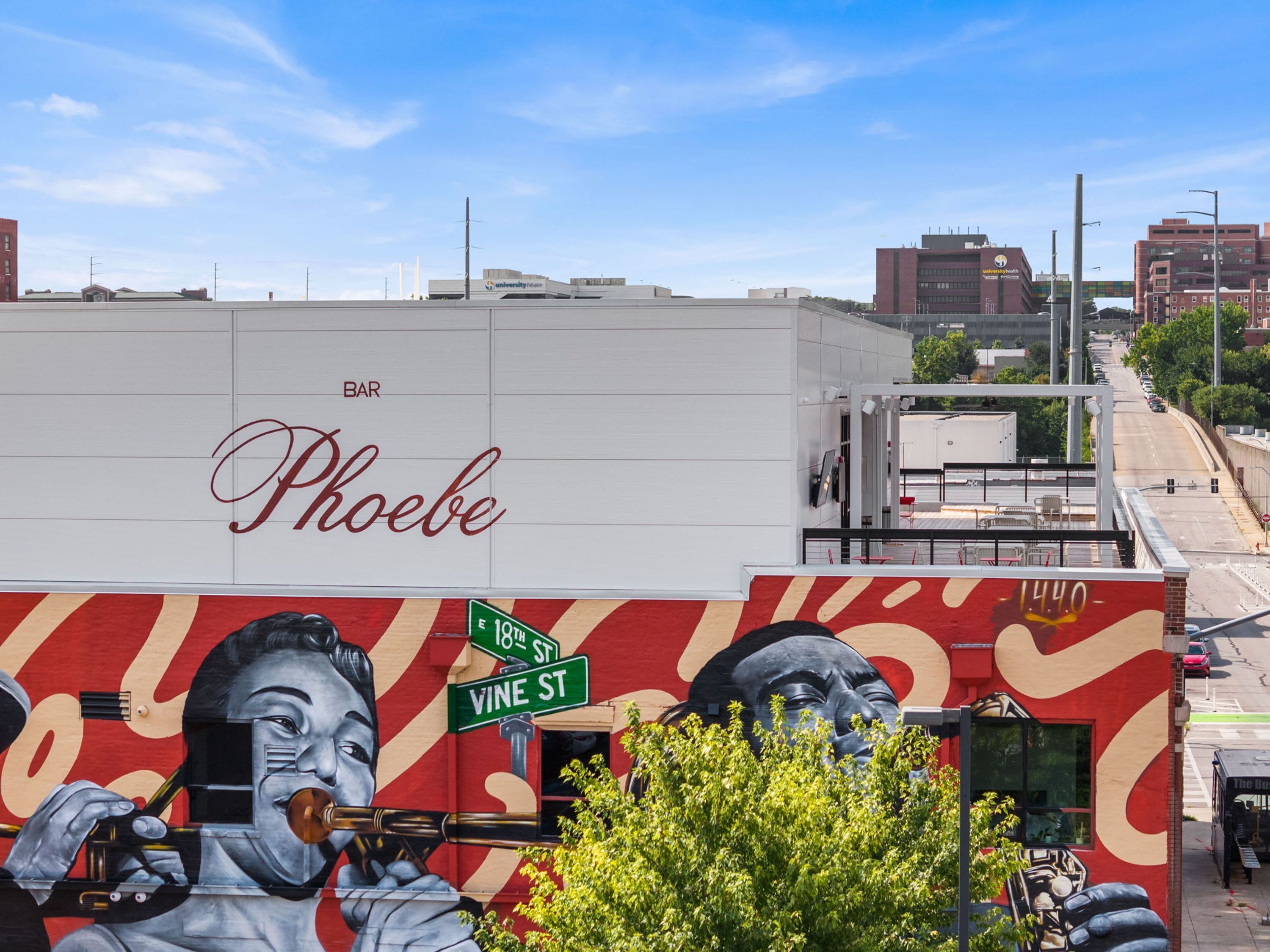 Ein Gebäude mit Wandgemälde eines Mannes, der Trompete spielt, Straßenschilder für Vine St und 18th St sowie eine Bar namens Phoebe.