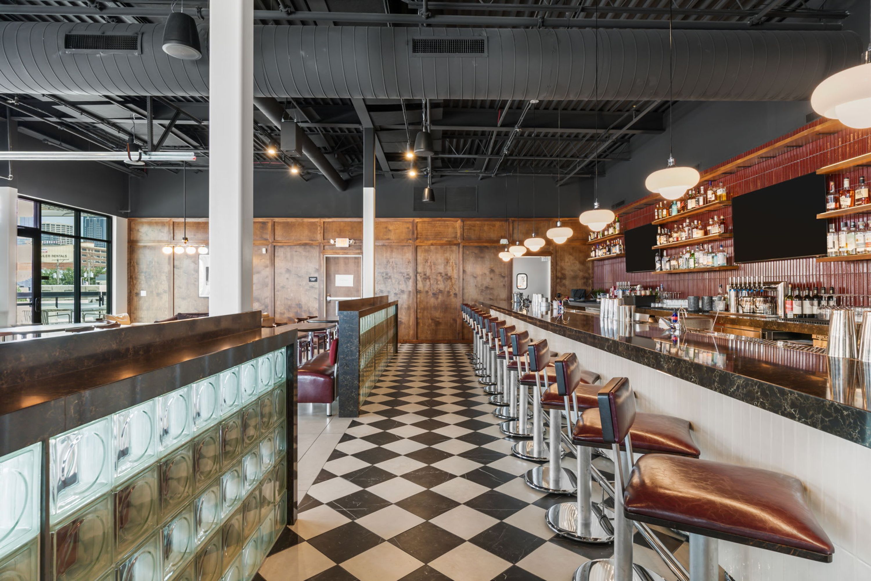 Un espace bar avec un sol à carreaux, des tabourets de bar et un comptoir où sont exposées des bouteilles.