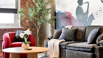 A living room with a red chair, a grey sofa, a wooden coffee table, and a large abstract painting.