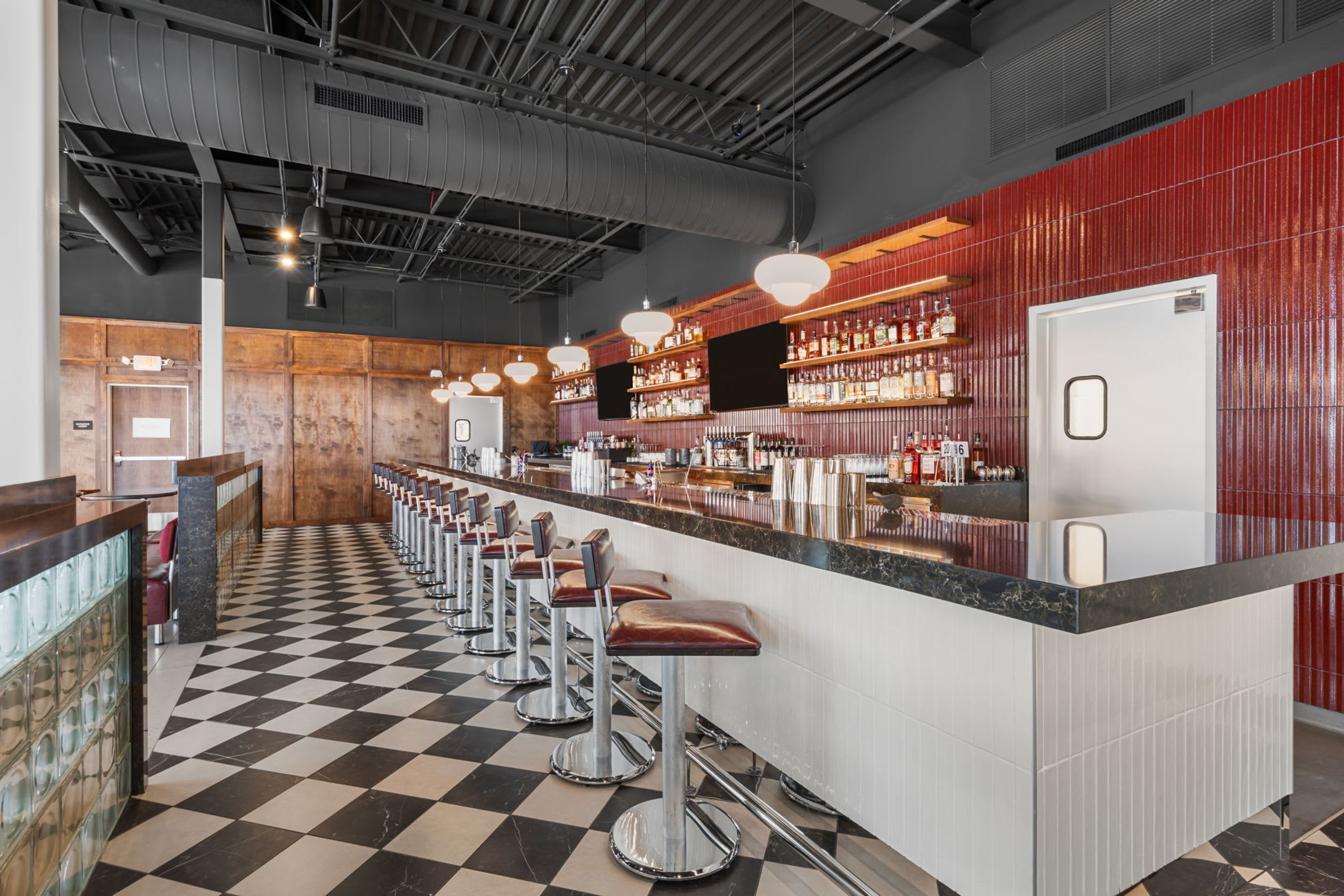 A bar area with a checkered floor, bar stools, and a counter with shelves of bottles.