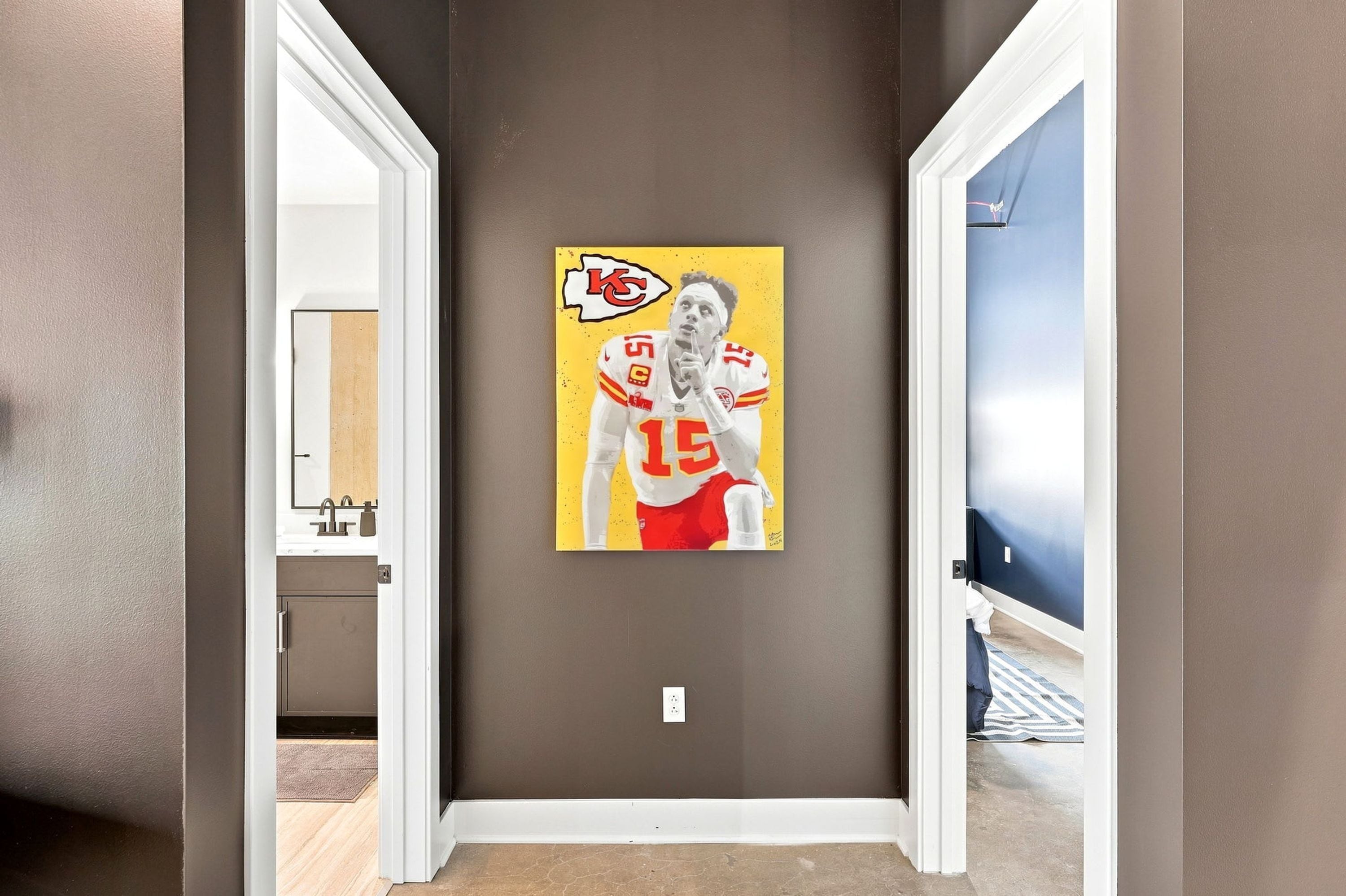 A hallway with a door leading to a bathroom, a wall-mounted artwork of a football player, and a visible light switch.