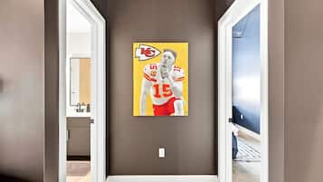 A hallway with a door leading to a bathroom, a wall-mounted artwork of a football player, and a visible light switch.