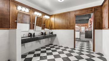 A public restroom with a checkered floor, wooden cabinets, and a mirror with lights.