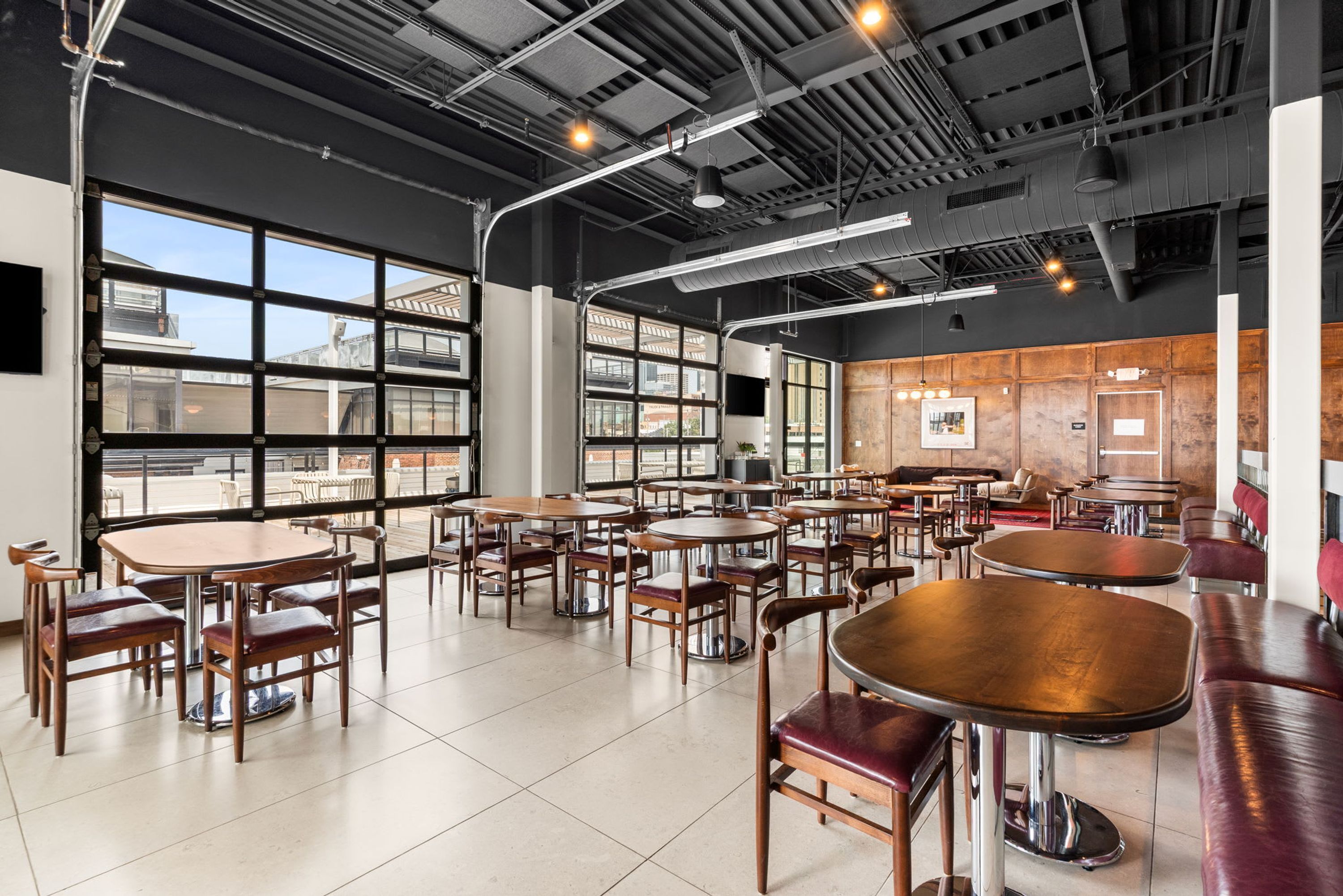 Un espace intérieur vaste et lumineux, avec de nombreuses tables et chaises, de grandes fenêtres et un plafond haut avec des poutres apparentes.