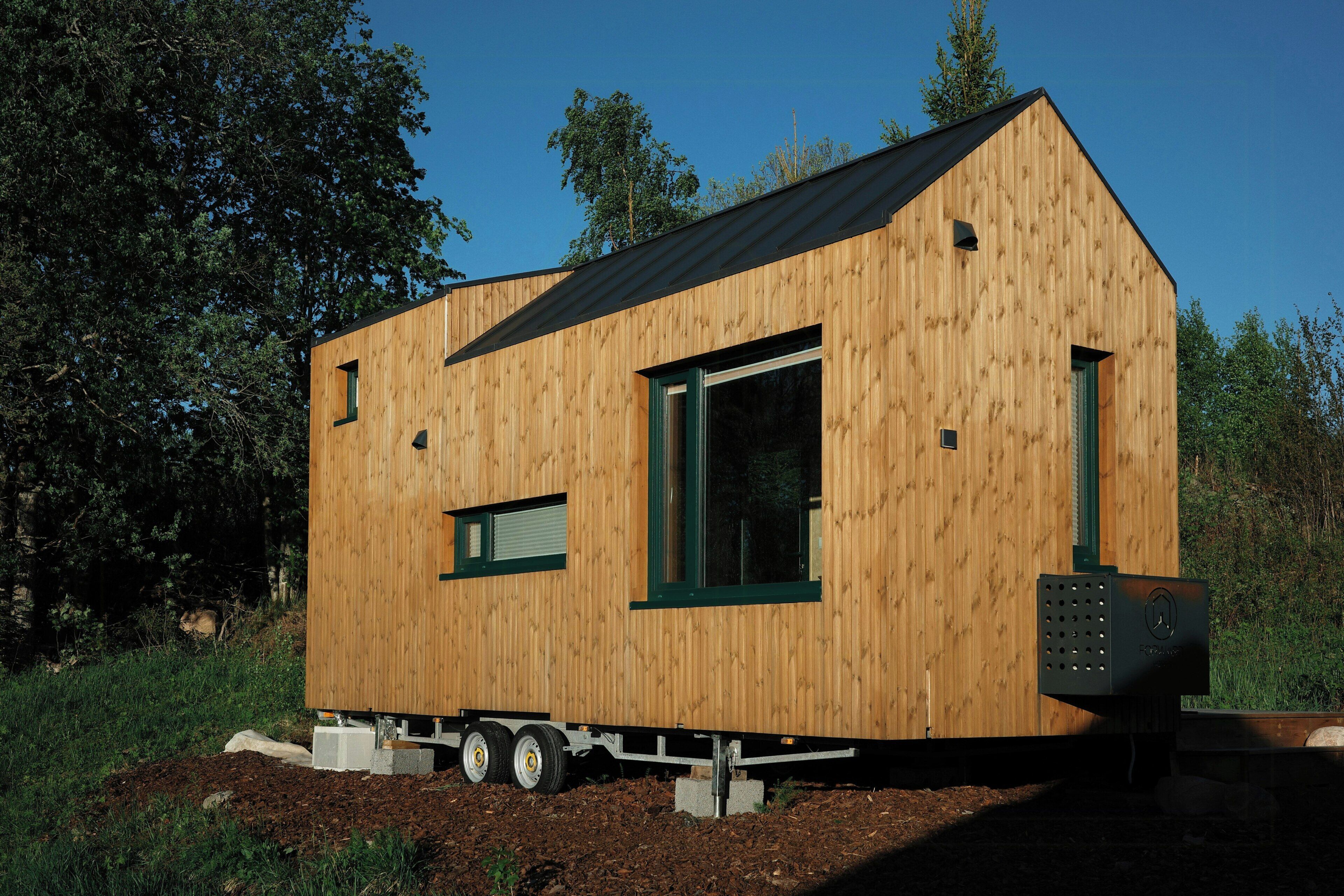Une maison mobile en bois, avec un toit noir, de grandes fenêtres et une petite structure attenante.