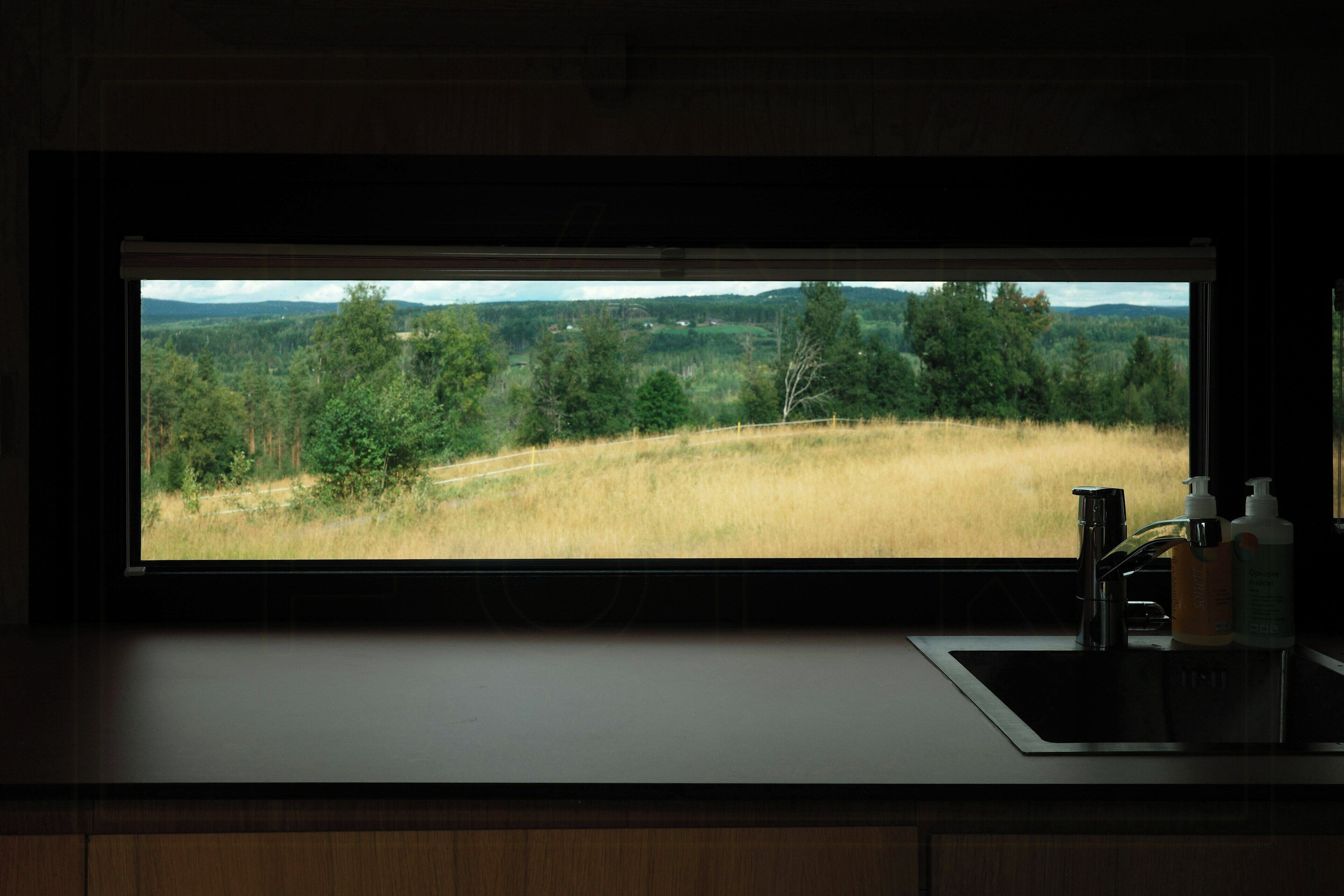 A kitchen with a large window overlooking a grassy landscape.