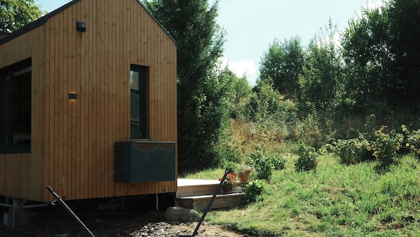 Une cabane en bois avec un toit en pente, une fenêtre et un petit espace de véranda agrémenté de plantes en pot.