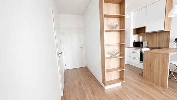 Ett modernt kök med träinredning, en inbyggd hyllsektion och en matplats med en vit stol.