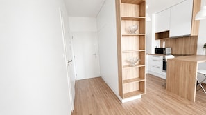 A modern kitchen with wooden cabinetry, a built-in shelf unit, and a dining area with a white chair.