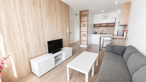 Ett modernt vardagsrum med en platt-TV, ett vitt soffbord och en grå soffa.