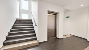 A modern interior with a staircase leading to an elevator, white walls, and a tiled floor. - AC 2 room apartment with terrace, Prievozska (Bratislava)