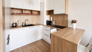 A modern kitchen with white cabinets, a wooden countertop, a built-in microwave, and a small potted plant.