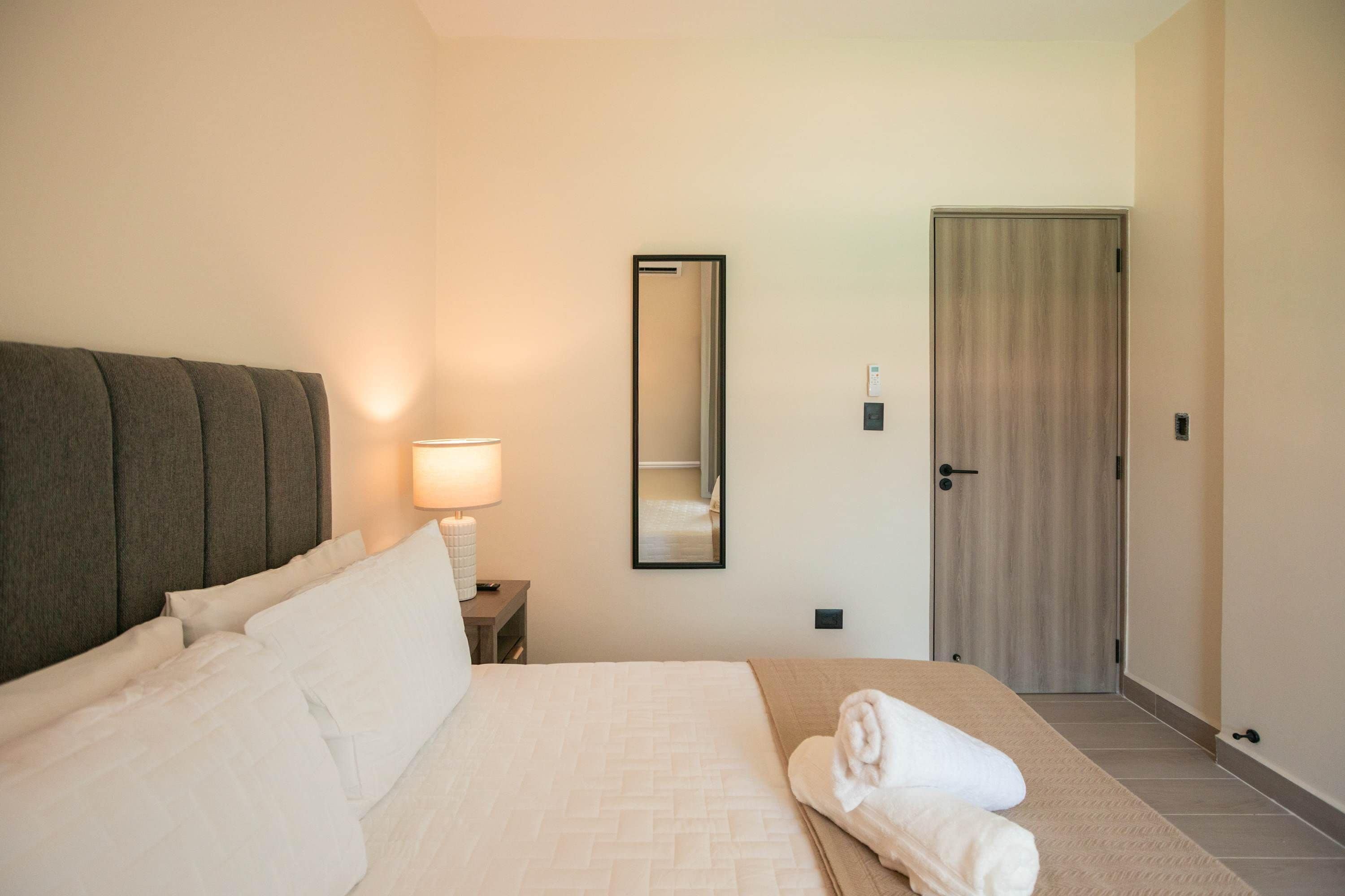 Une chambre d’hôtel avec un lit, une lampe de chevet, un miroir et une porte.