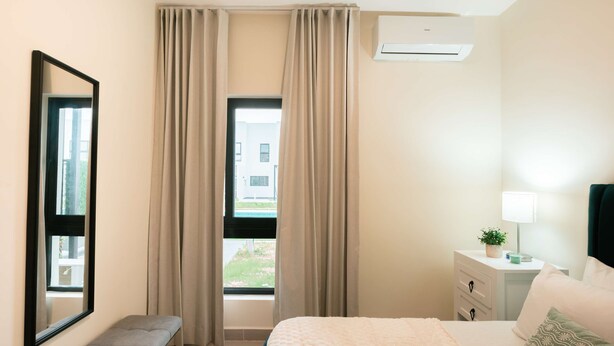 Habitación de hotel con cama, una banca, una mesita de noche con lámpara y una ventana con cortinas.