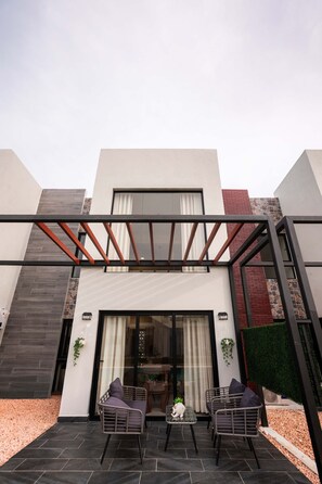 Ein modernes Haus mit überdachter Terrasse, zwei Stühlen, einem kleinen Tisch und einem Blumentopf.